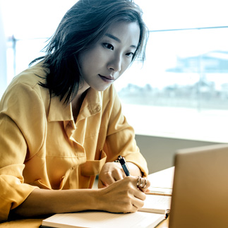 Photo of women writing in notebook while looking at laptop Photo of women writing in notebook while looking at laptop