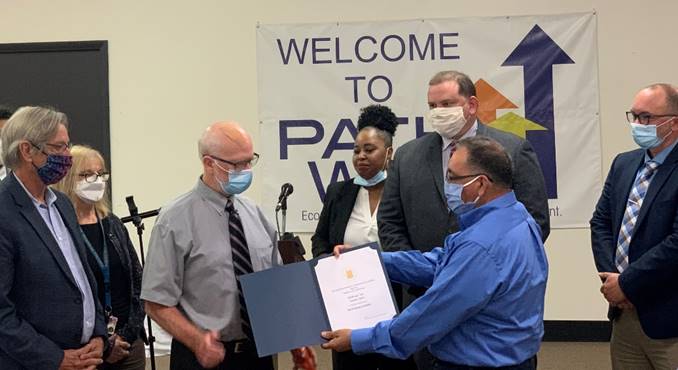 [(Left to right) Lucas County Commissioner Pete Gerken, Pathway interim CEO Robert Jordan, Pathway Director of Employment and Career Services Tomeka Rushing, Toledo Mayor Wade Kapszukiewicz, and Lucas Metropolitan Housing Authority President and CEO Joaquin Cintron Vega join HUD Midwest Regional Administrator Joseph P. Galvan as he presents the Pathway EnVision Center designation certificate and facilitates the ribbon cutting.]