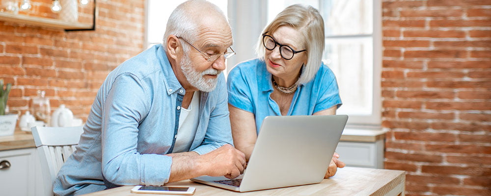 An older couple are looking at news on a laptop screen.